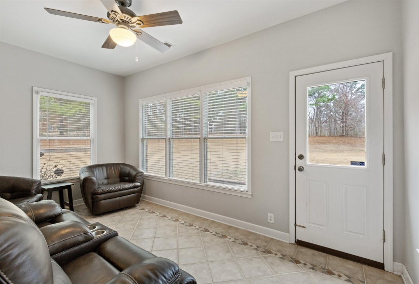 Bright room featuring multiple windows with blinds, a ceiling fan with integrated lighting, and tile flooring with a decorative border