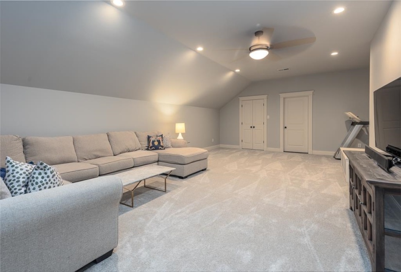 Spacious room featuring sloped ceilings, recessed lighting, and light-toned carpeting