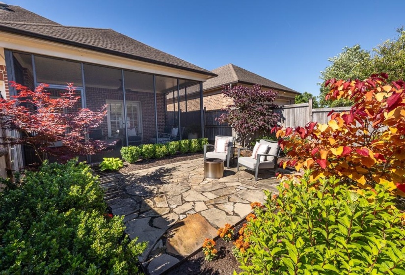 Screened porch with brick exterior, flagstone patio, mature landscaping, and privacy fencing