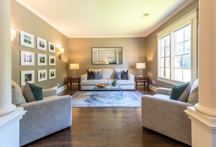 Formal living area featuring wood-finish flooring, patterned wall covering, crown molding, and two multi-pane windows