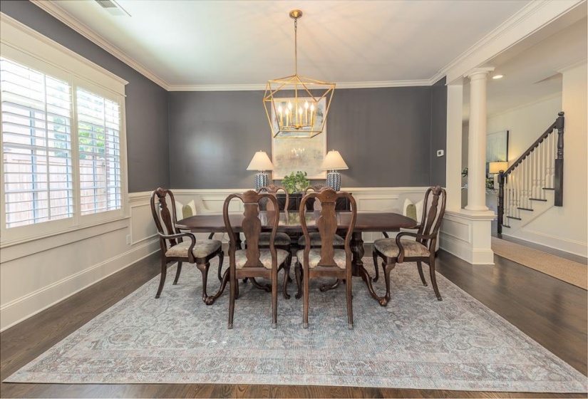 Formal dining room featuring dark wood-finish flooring, white wainscoting, and plantation shutters