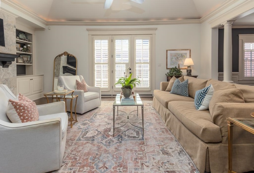 Sunlit room featuring French doors with interior plantation shutters, built-in cabinetry with open shelving, and decorative columns