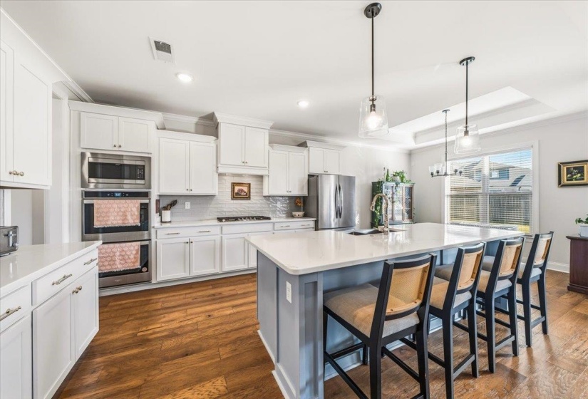 Kitchen featuring backsplash, a breakfast bar, pendant lighting, dark wood-style flooring, and crown molding