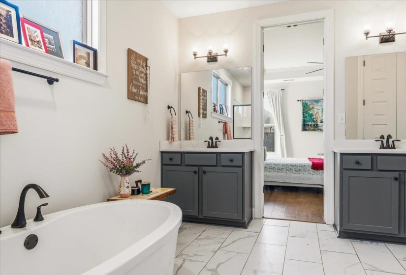 Bathroom featuring two vanities, light marble finish flooring, a freestanding bath, and connected bathroom
