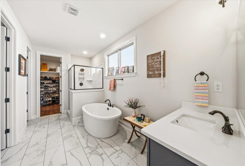Full bathroom with a stall shower, a freestanding bath, a spacious closet, vanity, and light marble finish floors