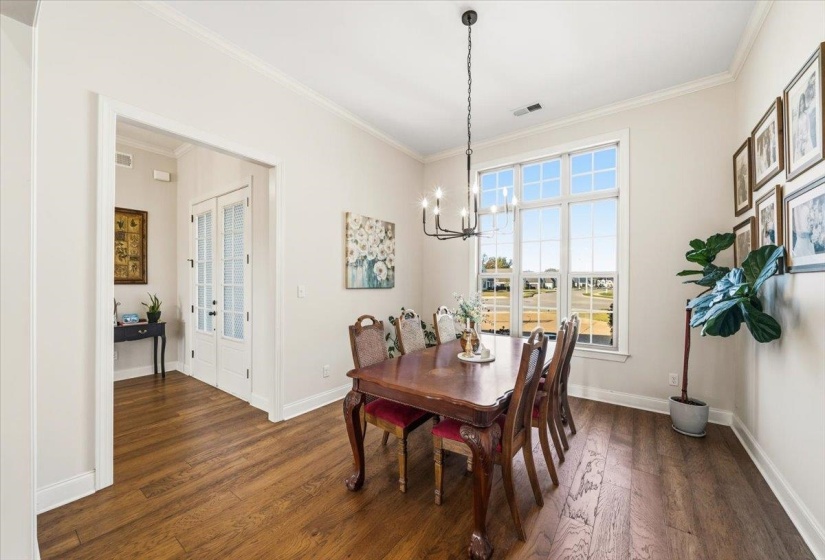 Dining room with dark wood-type flooring, crown molding, and a chandelier