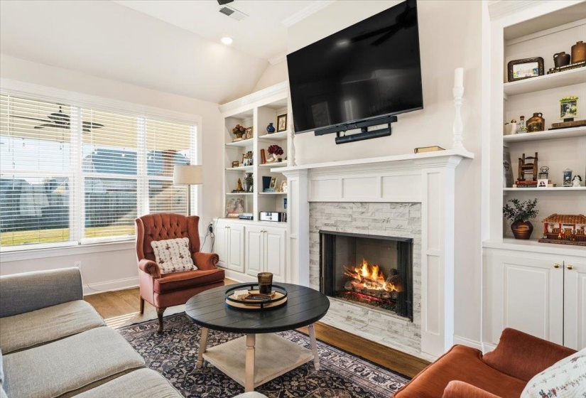 Living area featuring a premium fireplace, vaulted ceiling, wood finished floors, and built in features