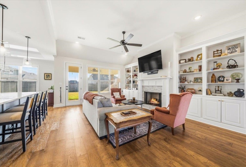 Living room with wood finished floors, a warm lit fireplace, ceiling fan, and recessed lighting