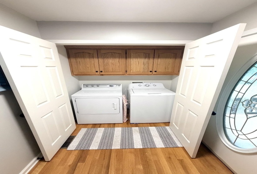 Dedicated laundry space featuring built-in wood cabinetry, a light gray wall color, and wood-finish flooring
