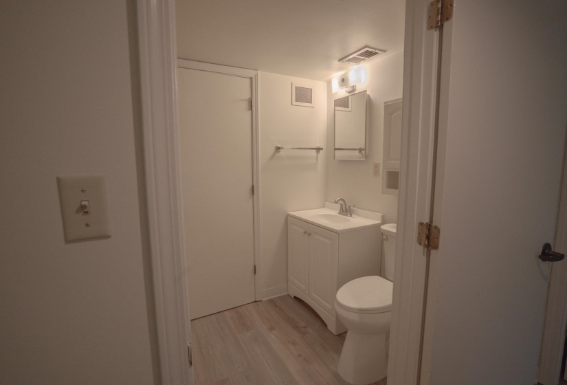 Compact bathroom featuring a white vanity with integrated sink, chrome faucet, wall-mounted medicine cabinet, and wood-finish flooring