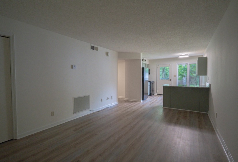 Open-concept living space with wood-finish flooring, white walls, and a dedicated dining area featuring a breakfast bar with a solid surface countertop