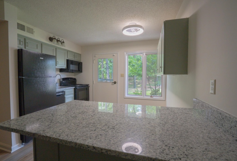 Kitchen featuring light-toned cabinetry, granite-style countertops, and a full suite of black appliances