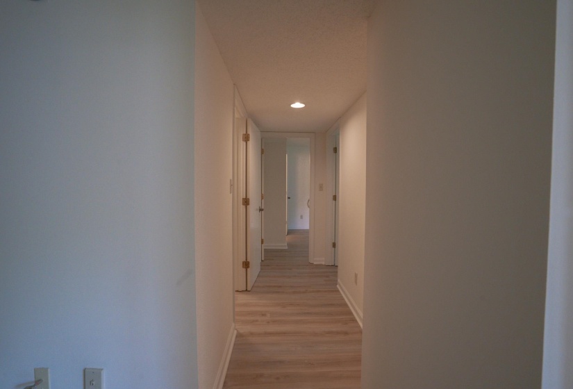 Hallway featuring wood-finish flooring, recessed lighting, and crisp white walls