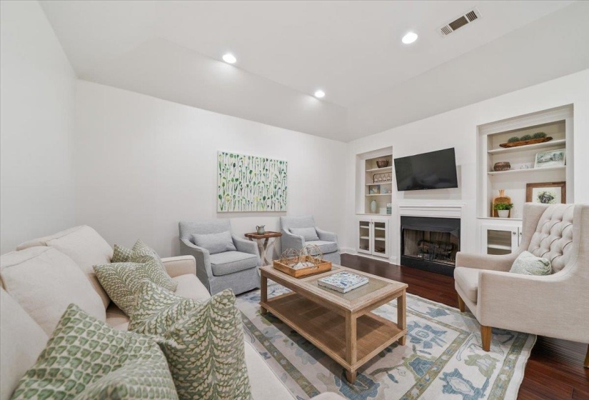 Living area featuring rich wood-finish flooring, recessed lighting, and a white fireplace surround