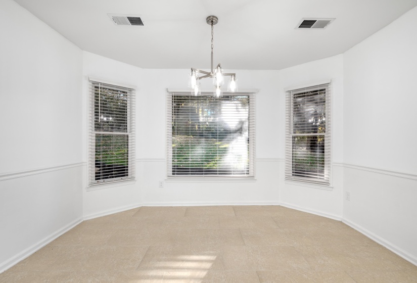 Bay window area featuring three windows with blinds, a ceiling-mounted light fixture, white wainscoting, and tile flooring