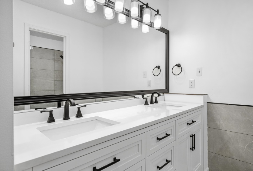 Dual sink vanity with white cabinetry and integrated sinks, matte black hardware, and a large framed mirror