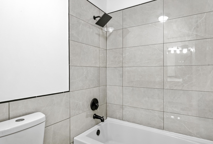 Bathtub and shower combination featuring black matte fixtures and light gray tiled walls