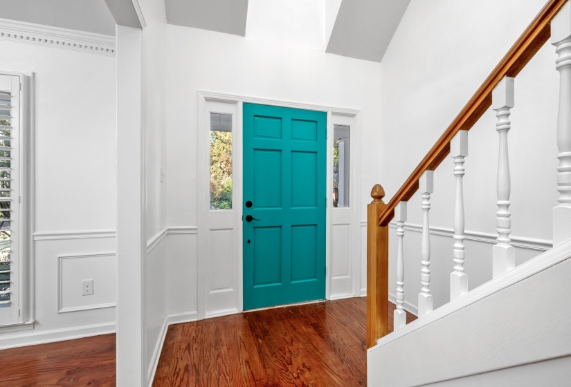 Vibrant turquoise front door with side lites, hardwood flooring, wainscoting details, white trim throughout, and a wood handrail