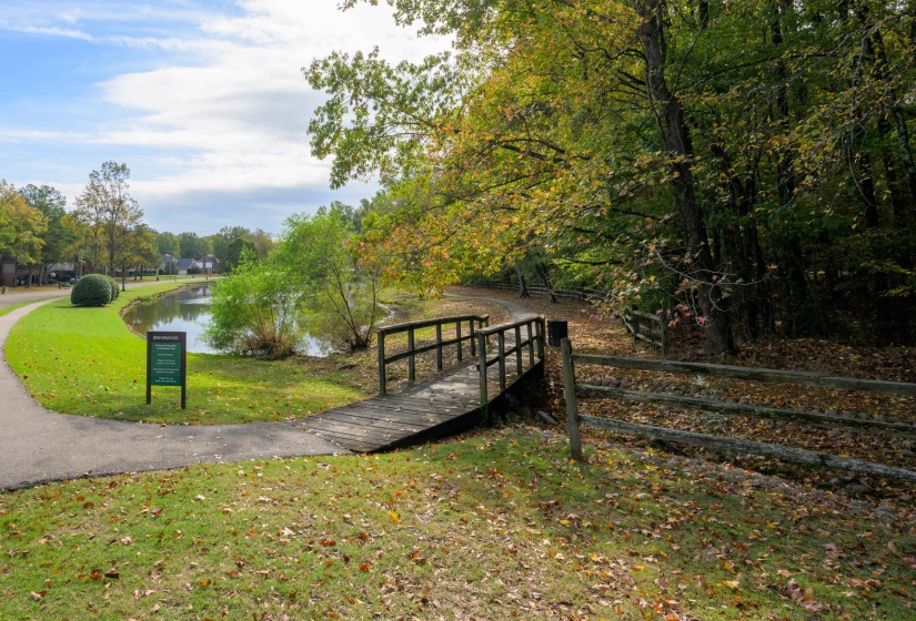 Serene pond with a water feature, bordered by a paved walking path and mature trees