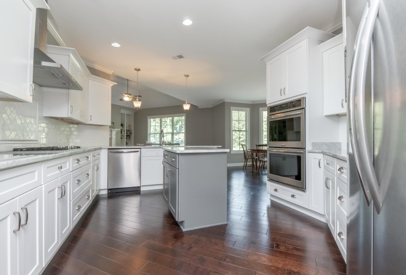 Spacious kitchen featuring white shaker cabinetry, stainless steel appliances, a central island with a contrasting base, wood-finish flooring, and a subway tile backsplash