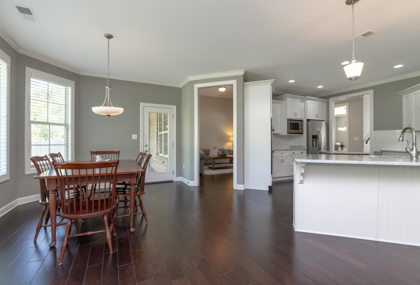 Open-concept dining area featuring dark wood-finish flooring, a contemporary ceiling light fixture, and crown molding