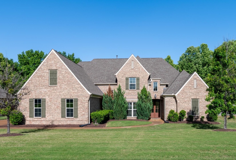 Brick facade residence featuring a multi-gabled roofline, green window shutters, a prominent entry porch, and mature landscaping