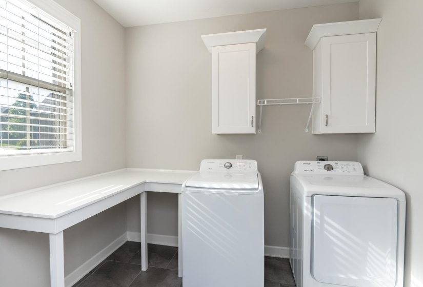 Laundry room featuring a white built-in L-shaped countertop, white upper cabinetry, and window with blinds