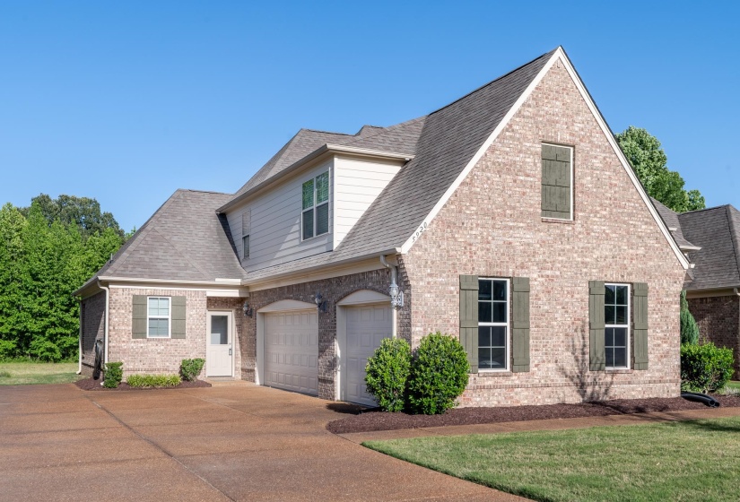 Brick and siding exterior featuring gabled rooflines, a two-car garage with arched entries, and a wide paved driveway
