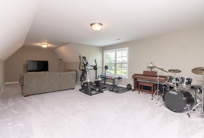 Spacious room featuring light-colored carpeting, sloped ceilings, and recessed lighting fixtures