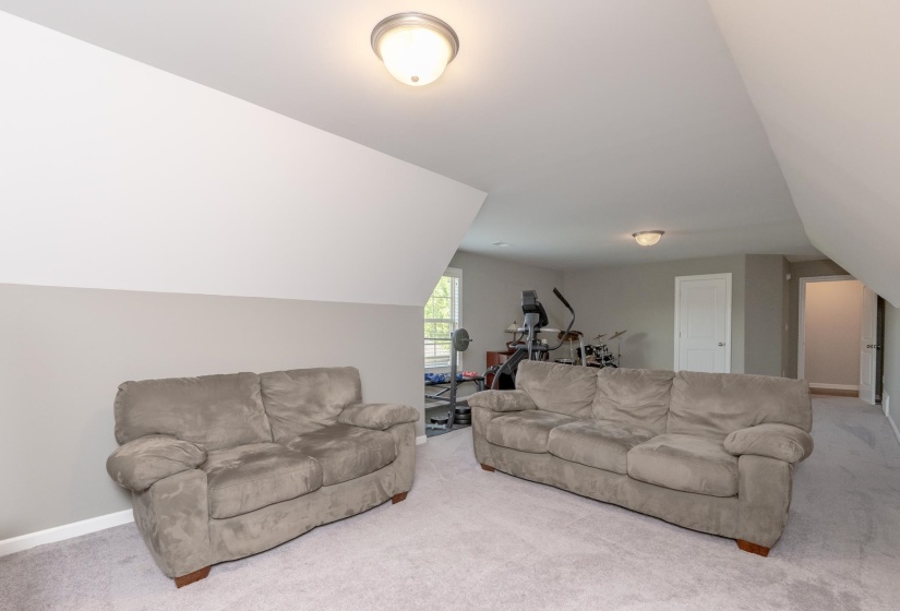 Spacious carpeted room featuring angled ceilings, neutral wall tones, and recessed lighting