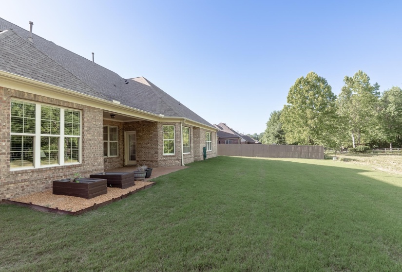 Expansive rear lawn featuring a privacy fence, mature trees, and a brick exterior with a covered patio