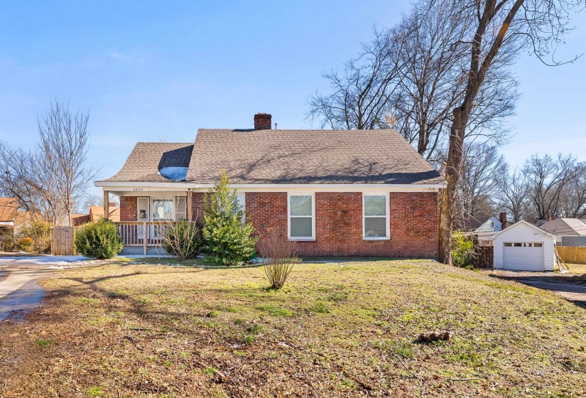 View of front of property featuring brick siding, a chimney, roof with shingles, and covered porch