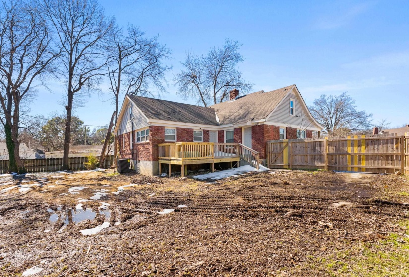 Back of house featuring a fenced backyard, a wooden deck, brick siding, and a chimney