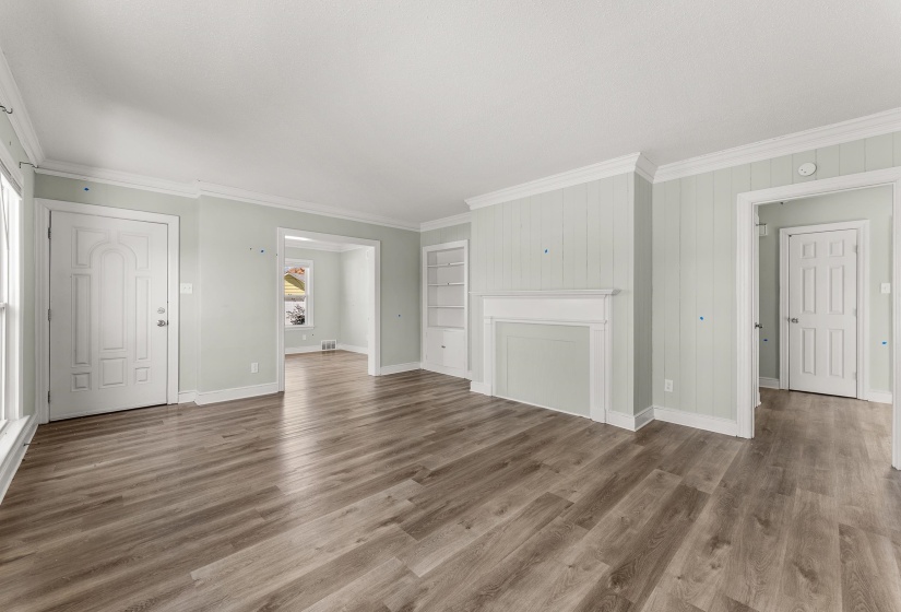 Unfurnished living room featuring built in shelves, wood finished floors, and crown molding