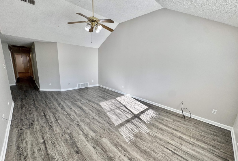 Spacious room featuring vaulted ceilings, wood-finish flooring, a ceiling fan with integrated lighting, and neutral wall tones
