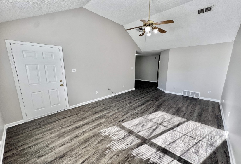 Spacious interior featuring wood-finish flooring, vaulted ceiling, and a ceiling fan with integrated lighting