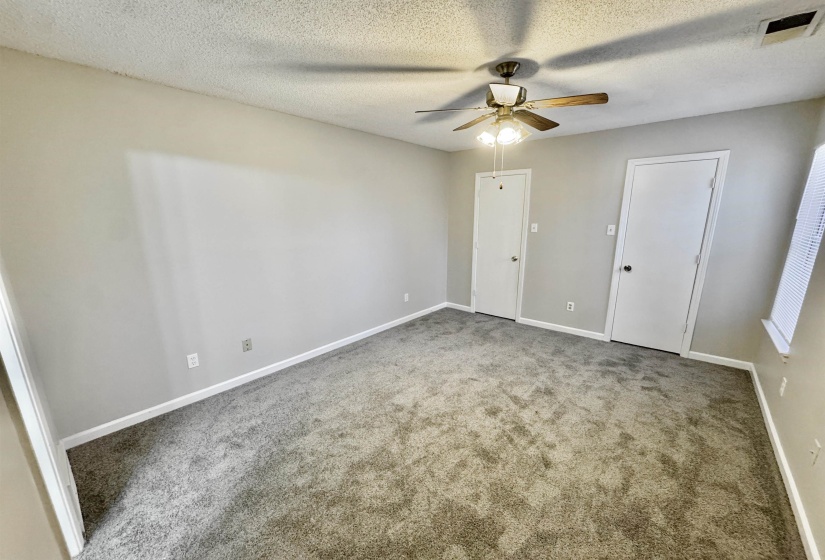 Spacious room featuring new carpeting, freshly painted walls, white trim, a ceiling fan with light fixture, and multiple white panel doors