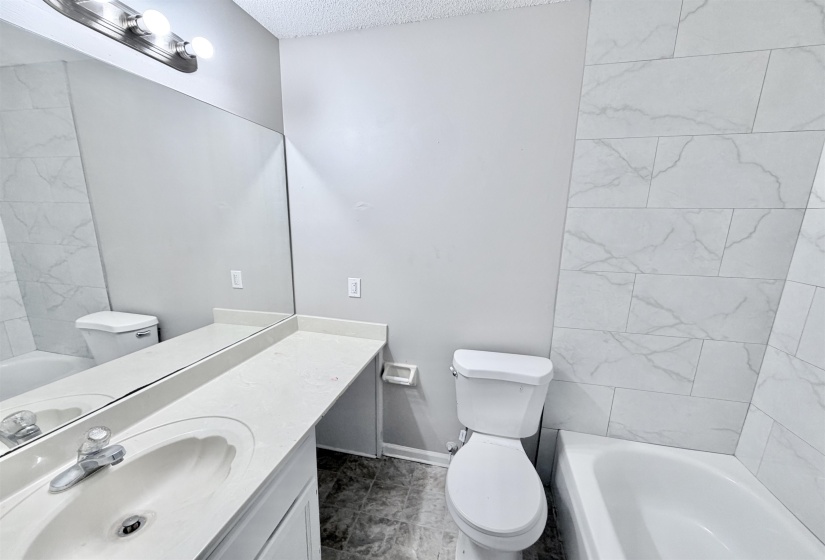Bathroom featuring a vanity with an integrated sink and light countertop, an expansive wall mirror, and a full bathtub with tile surround