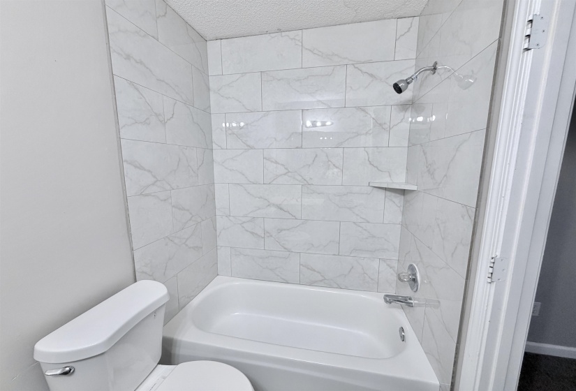 Bathtub and shower combination featuring white subway tile surround with subtle gray veining, chrome shower head, and chrome tub filler