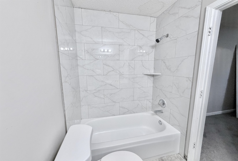 Bathroom featuring a white bathtub, chrome fixtures, and a shower surround with white marbled tile