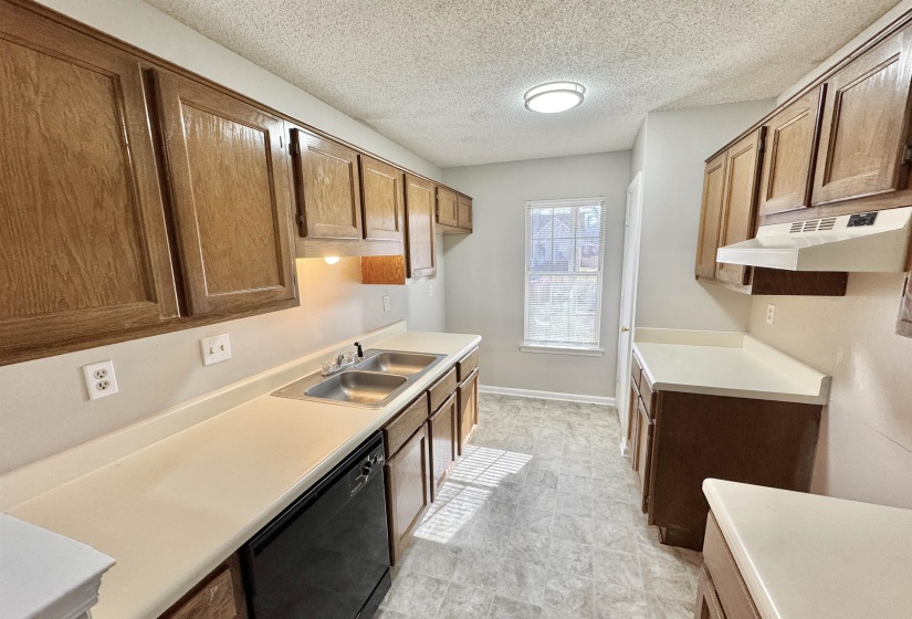 Kitchen featuring wood cabinetry, light-toned countertops, a double basin stainless steel sink, and a built-in dishwasher