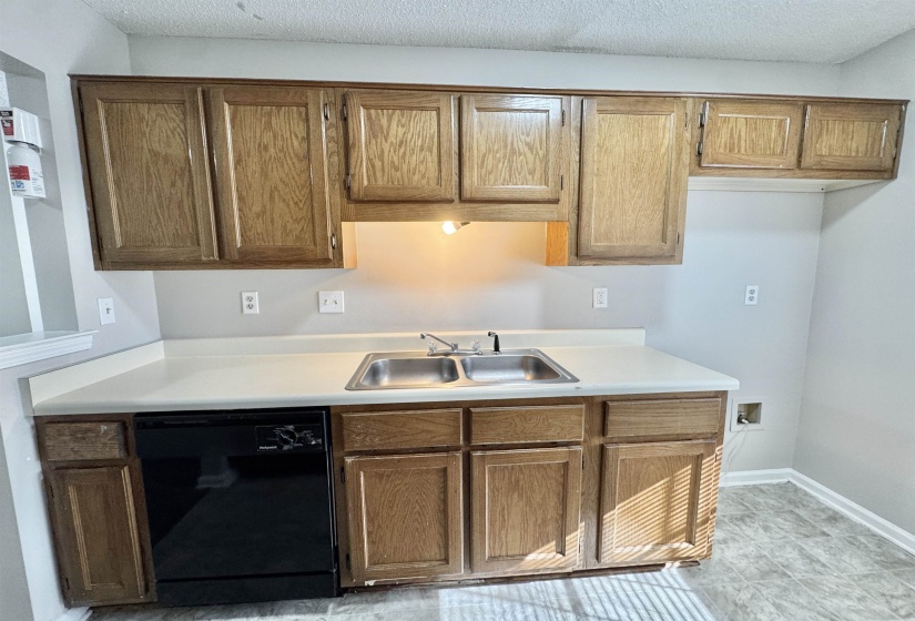 Kitchen area featuring light wood-finish cabinetry, a double-basin stainless steel sink, and light-colored countertops