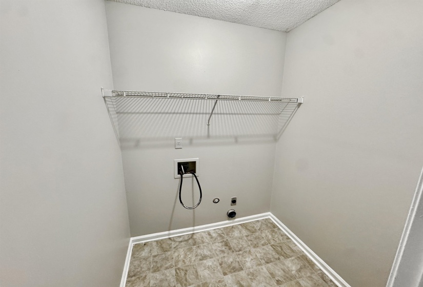 Laundry area featuring a wire storage shelf, light gray walls, and patterned vinyl flooring