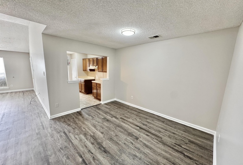 Open concept living area featuring wood-finish flooring, neutral wall tones, and a kitchen pass-through with wood cabinetry