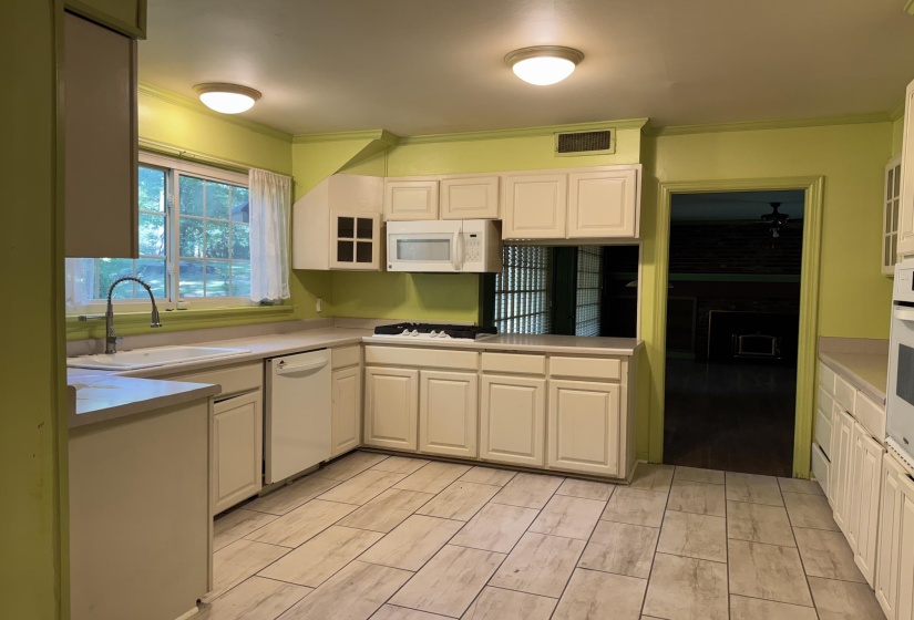 Kitchen featuring L-shaped cabinetry, light-toned countertops, and a white sink with an arched faucet