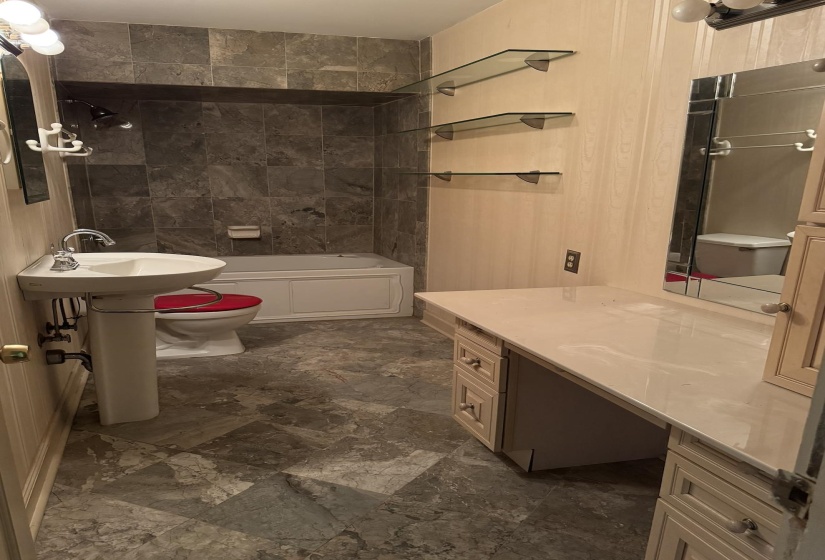 Bathroom featuring a pedestal sink, tiled shower surround, recessed bathtub, vanity with integrated countertop, and an accent mirror
