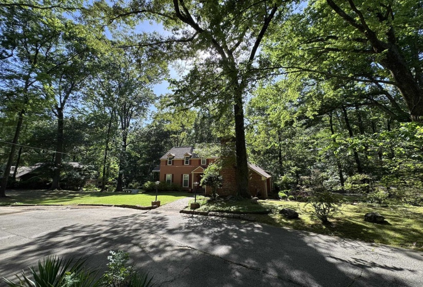 Brick residential structure with dormer windows and a gabled roofline, situated amidst mature trees