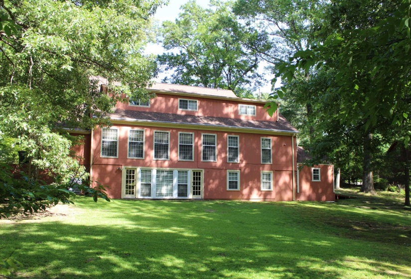 Spacious rear exterior featuring an expansive lawn, multiple windows, and a dormer roof