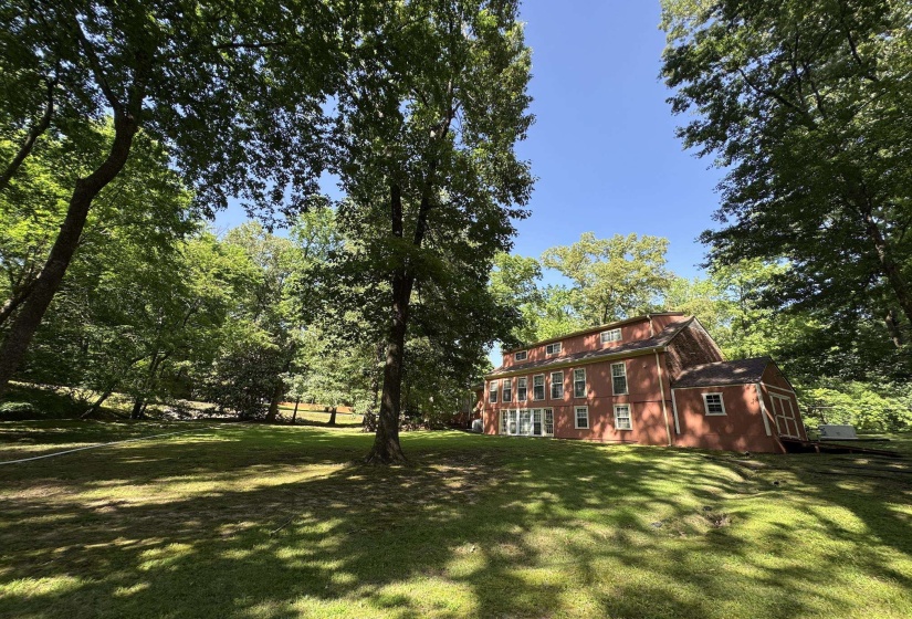 Expansive green lawn with mature trees surrounding a multi-story red exterior residence featuring multiple windows and a gabled roofline
