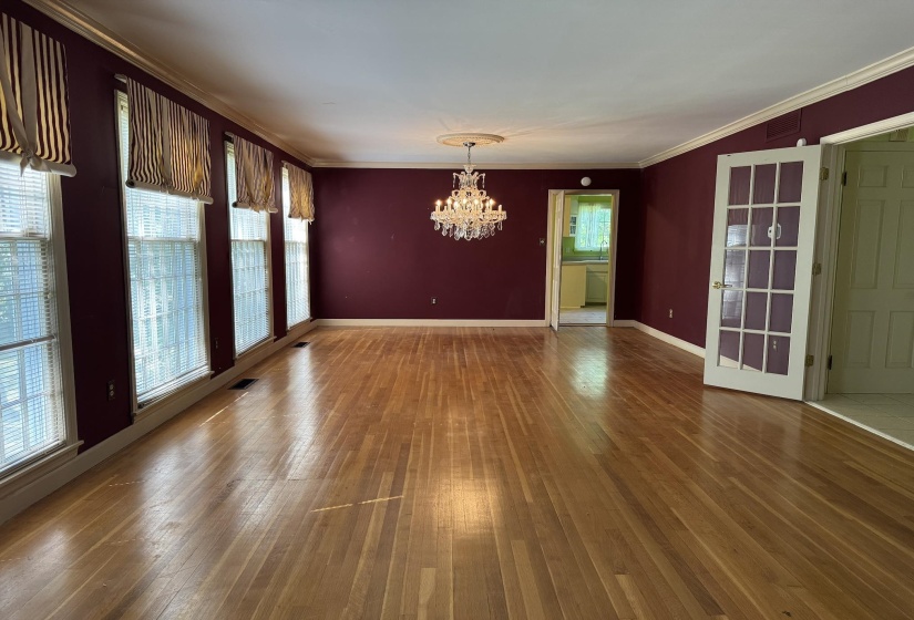Hardwood flooring and crown molding define this room featuring multiple windows with blinds, a crystal chandelier, and French doors